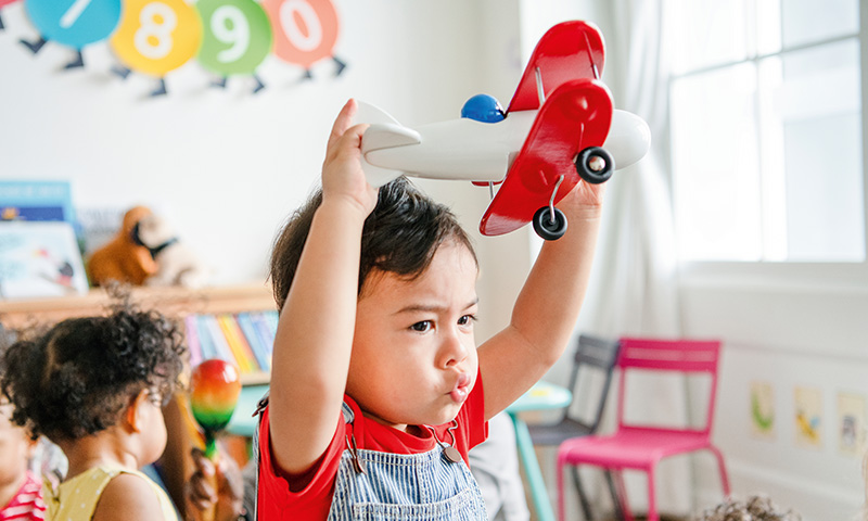Zufriedener Junge in Kindergarten mit Spielzeug-Flugzeug